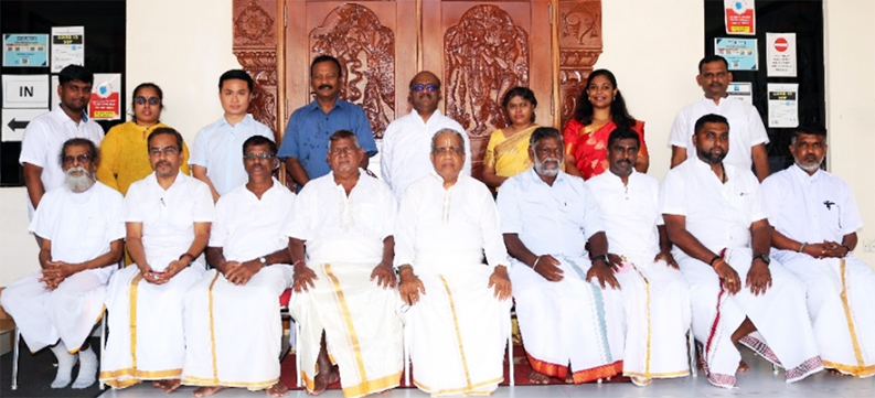 person writing in a notebook beside by an iPad, laptop, printed photos, spectacles, and a cup of coffee on a saucer